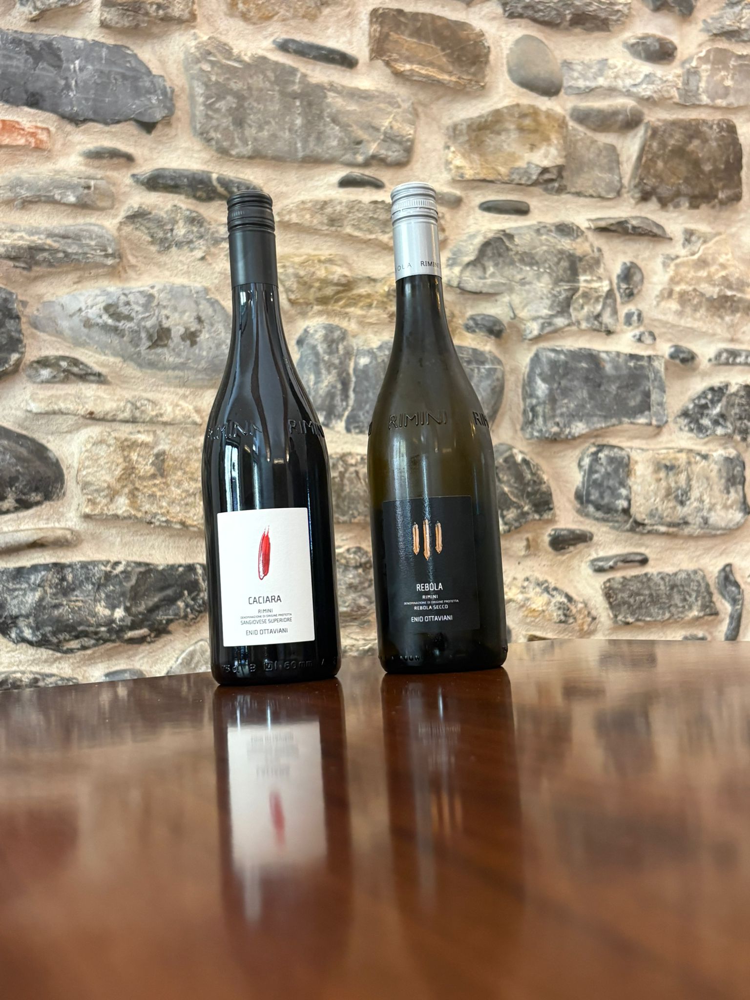 Two wine bottles on a table in front of a stone wall
